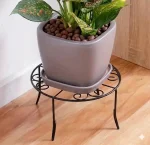 Modern circular Metal Plant Stand Pakistan with wood shelf holding an orange flower pot stand.
